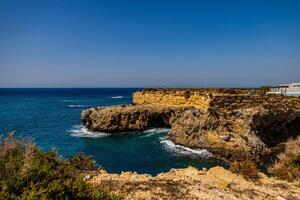 A rugged coastline with steep cliffs overlooks a calm, deep blue sea under a clear sky photo