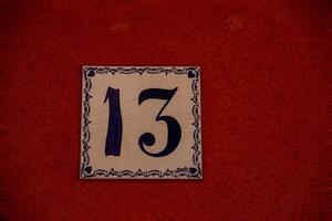 A ceramic tile with the number 13 is mounted on a textured, reddish-brown wall. photo