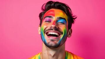 Joyful young man with vibrant rainbow face paint on bright pink background photo