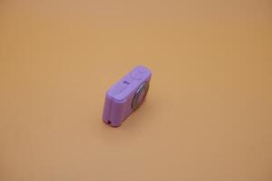 Small Purple Camera Toy on Beige Surface with Soft Shadows photo