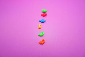 Plastic Toy Dinosaurs in Various Colors on Pinkish Background photo