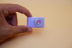 Compact Toy Camera Held Between Fingers on Neutral Backdrop photo
