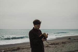 Man Flipping The Pages Of The Bible Book While Praying Near The Ocean Stormy photo