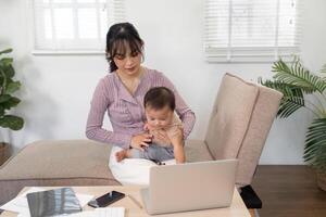 Engaged mother interacting with her baby while working on a laptop at home photo