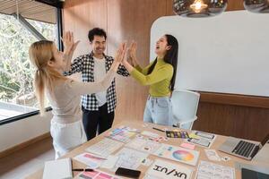 Excited colleagues high-fiving in a bright workspace, emphasizing teamwork and creativity. photo