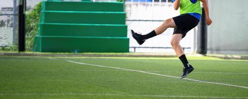 Soccer player kicking ball on green artificial turf field during practice with green bleachers and goalpost in background, showing action and movement photo