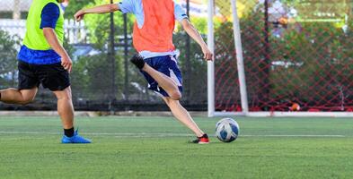 Soccer players in action during game on grass field focusing on their legs and ball with vibrant jerseys and goal net in background creating energetic sports scene photo
