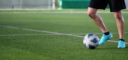 Soccer player wearing blue cleats controlling ball on green grass field during game, focusing on legs and ball in action with blurred goalpost in background photo