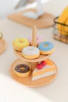 Close up view of colorful donuts with sprinkles on wooden stand featuring slice of cake creating delightful and tasty presentation in bright setting photo
