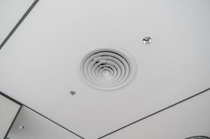 Clean modern office ceiling featuring circular air vent, recessed lighting, and grid pattern with white panels and dark trim creating sleek and functional design photo