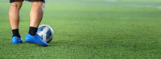 Soccer player standing on green grass field with blue cleats and black socks, focusing on ball near feet during game or practice session photo
