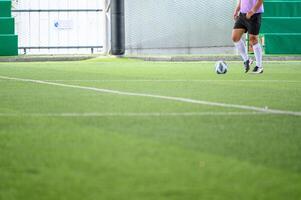 Soccer player wearing white socks and black shorts is about to kick ball on green artificial turf field inside indoor sports facility with netted walls photo