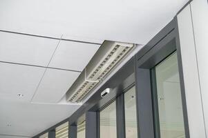 Close up view of modern office ceiling featuring built in air vent unit and sleek design with glass windows and metal frames creating clean and professional atmosphere photo