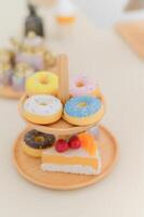Close up view of colorful donuts with sprinkles on wooden stand featuring slice of cake creating delightful and tasty presentation photo