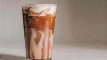 A tall glass of chocolate milk with white cream swirls on a white background wall photo