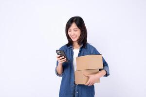 Southeast asian woman shopping online happily holds two cardboard boxes while checking her phone for orders or delivery updates in bright studio setting photo