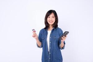 Southeast asian woman happily uses mobile phone and internet application while holding credit card for online shopping or payment in casual denim shirt on white background photo