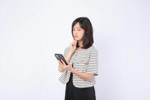 Southeast asian woman uses mobile phone with internet application looking thoughtful and focused on white background in casual striped jacket and black dress photo