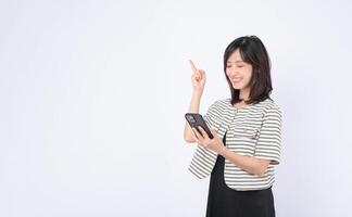 Southeast asian woman happily uses mobile phone to explore internet application while pointing upward with her finger in bright studio setting photo