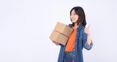 Southeast Asian woman shopping online holds two cardboard boxes and shows thumbs up with happy smile expressing satisfaction and confidence in her purchase experience photo