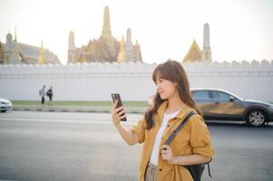 Southeast asian woman enjoys travel concept by taking selfie with smartphone near historic temple in warm sunlight creating joyful and peaceful moment outdoors photo