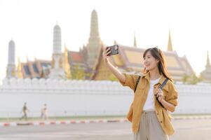 Southeast asian woman travel concept captures joyful woman taking selfie with historic temple background during her travel adventure in bright and warm atmosphere photo