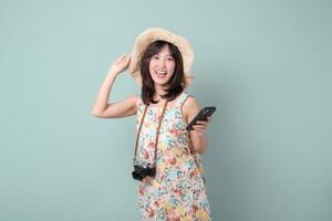 Southeast asian woman joyfully uses mobile phone to explore internet application while wearing floral dress and straw hat with camera hanging around her neck photo
