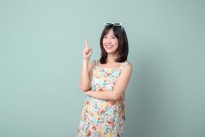 Southeast asian woman shopping online looks happy and confident while pointing upward wearing floral dress and sunglasses on her head against plain background photo