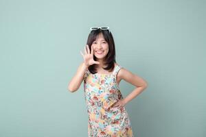 Southeast asian woman in colorful dress smiling and gesturing with hand near face, standing against light green background, cheerful and friendly expression photo