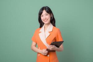 Southeast Asian woman smiling while holding tablet, standing against green background, representing internet technology and modern communication in professional setting photo