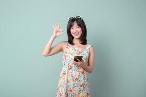 Southeast asian woman holding smartphone showing ok gesture with happy expression while using internet for online shopping against pastel background photo