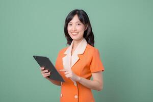 Southeast asian woman in orange suit smiling and holding tablet against green background, showing confidence and modern technology use in professional setting photo