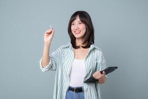 Southeast asian woman holding tablet and stylus smiling while using internet technology for creative work against plain background photo