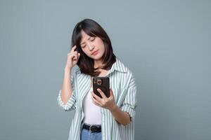 Southeast Asian woman using internet on smartphone looking confused while standing against plain background thoughtful expression photo