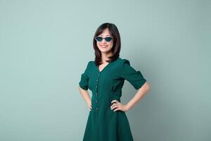 Southeast asian woman wearing sunglasses and green dress smiles confidently in this advertising style portrait with soft green background photo