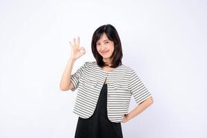 Southeast asian woman smiling confidently and making okay gesture for advertising with striped jacket and black dress on white background photo