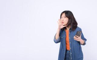 Southeast asian woman holding smartphone and whispering secret with advertising gesture on white background photo