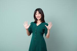 Southeast Asian woman in green dress smiling and showing ten fingers for advertising with happy and confident expression on light blue background photo