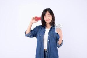 Southeast asian woman holding credit card and cash with confused expression using mobile internet application for payment or shopping decisions in casual denim clothing photo