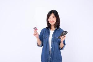 Southeast Asian woman holding mobile phone and credit card smiling while using internet application for online shopping or payment in casual denim shirt on white background photo