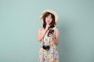 Southeast asian woman wearing hat looks thoughtfully at her mobile phone while holding camera around her neck using internet application for travel planning or communication photo