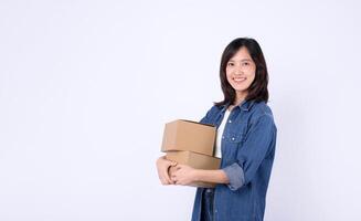 Southeast asian woman is happily shopping online and holding two cardboard boxes while standing against plain white background in casual denim clothing photo