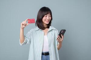Southeast asian woman shopping online happily holding credit card and smartphone with casual striped shirt and jeans on gray background photo