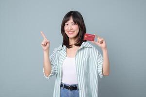 Southeast asian woman shopping online with credit card smiling and pointing up on gray background showing happiness and confidence photo