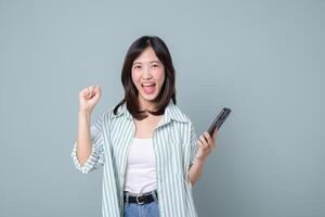 Happy southeast asian woman using mobile phone with internet connection enjoying mobile application in casual clothes with cheerful expression on plain background photo