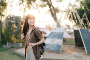 Southeast asian woman enjoys travel concept outdoors with joyful smile wearing casual clothes and carrying backpack in sunny park setting during golden hour photo