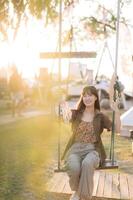 Southeast asian woman enjoys travel concept sitting on swing outdoors with warm sunlight creating joyful and relaxed atmosphere in natural park setting photo