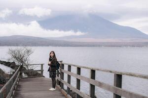 Southeast asian woman enjoys travel concept by standing on wooden bridge near calm lake with mountain covered in clouds in background creating peaceful atmosphere photo