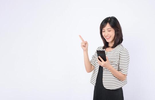 Southeast asian woman happily using mobile phone to explore internet application while pointing upwards with her finger in bright studio setting photo