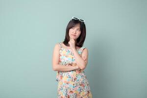 Southeast asian woman in colorful floral dress poses thoughtfully for advertising against plain light green background with sunglasses on her head photo